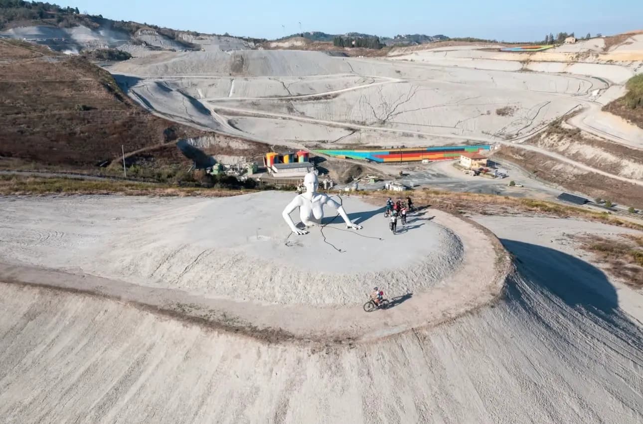 Aerial view of riders beside a Giant of Peccioli, with the colourful Green Triangle installation on the Belvedere behind