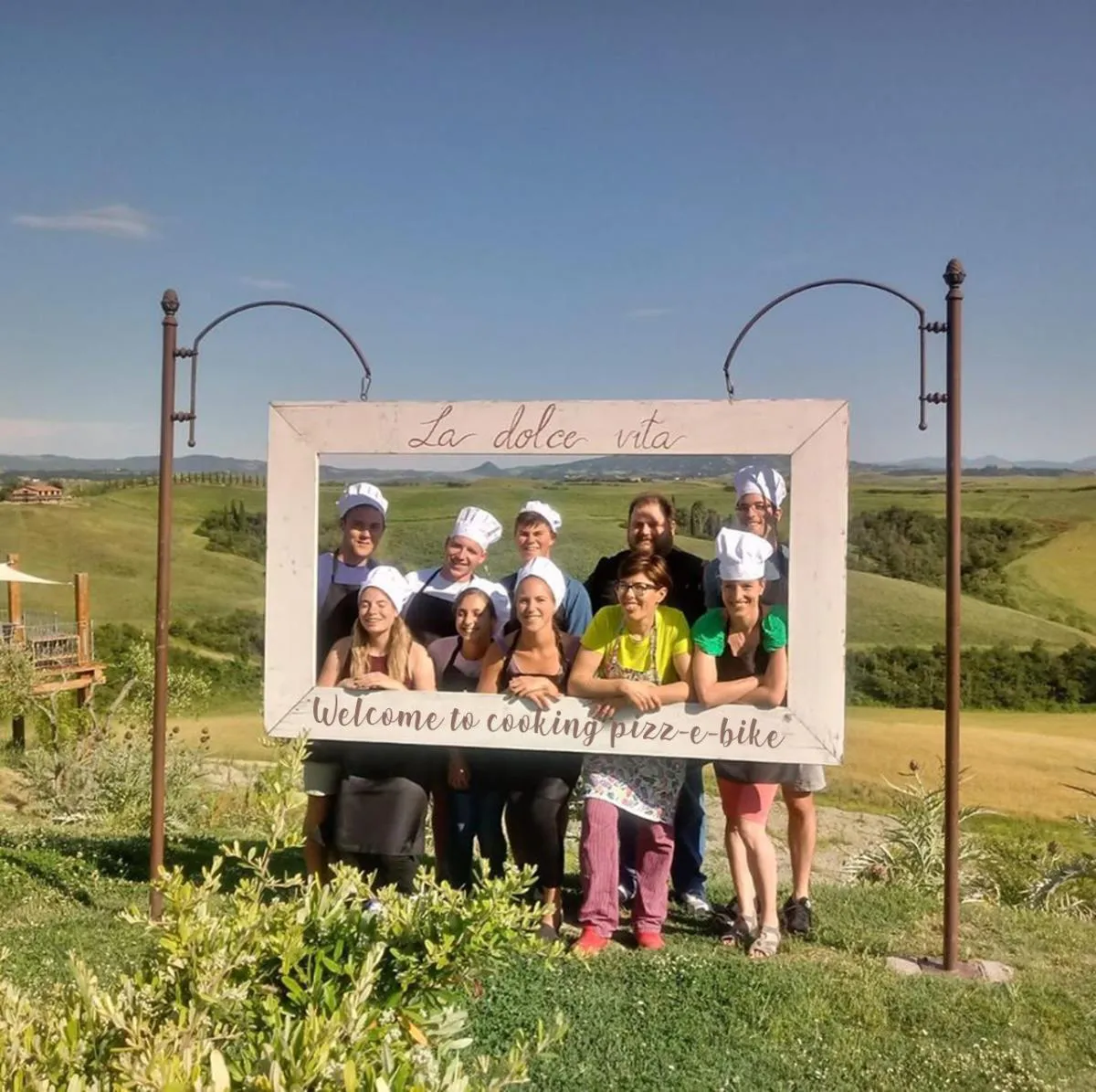 Happy group in chef hats at the Pizz-e-bike farm, Tuscan hills behind
