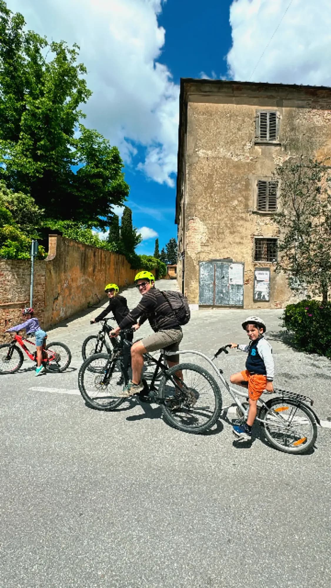 Family on e-bikes, including a child, riding through a Tuscan village
